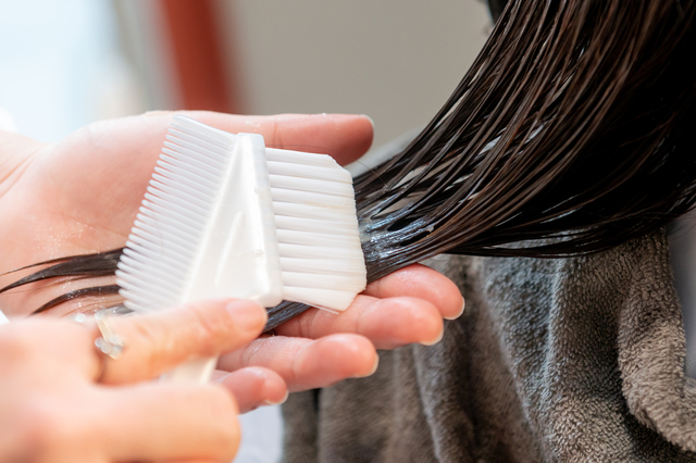 艶のあるブラウン系ヘアカラーの仕上がりを横顔越しに見せた自然光のクローズアップ